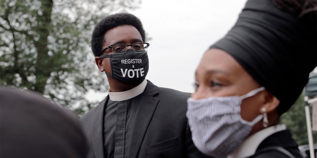 FILE - In this Monday, July 20, 2020 file photo, the Rev. Rahsaan Hall, of the St. Paul AME Church in Cambridge, Mass., wears a mask which reads, "Register & Vote" outside the Statehouse in Boston. (AP Photo/Charles Krupa)
