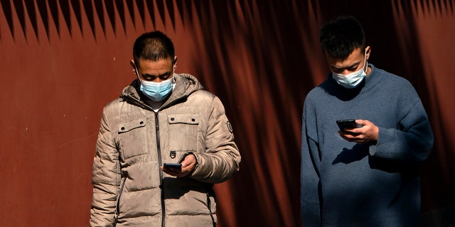 People wearing face masks to protect against the spread of the coronavirus use their smartphones as they walk through Ditan Park in Beijing, Tuesday, Feb. 9, 2021. China's internet watchdog is cracking down further on online speech, issuing a new requirement that bloggers and influencers have a government-approved credential before they can publish on certain topics. (AP Photo/Mark Schiefelbein)