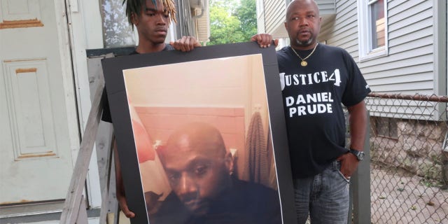 FILE - In this Sept. 3, 2020, file photo, Joe Prude, brother of Daniel Prude, right, and his son Armin, stand with a picture of Daniel Prude in Rochester, N.Y. (AP Photo/Ted Shaffre, File)