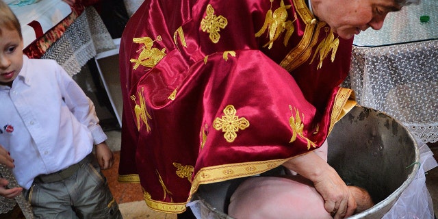 A picture taken on May 11, 2014 shows a Romanian Orthodox priest sinking a child in holy water during baptism, in a church in Bucharest. (Photo by Daniel MIHAILESCU / AFP) (Photo by DANIEL MIHAILESCU/AFP via Getty Images)
