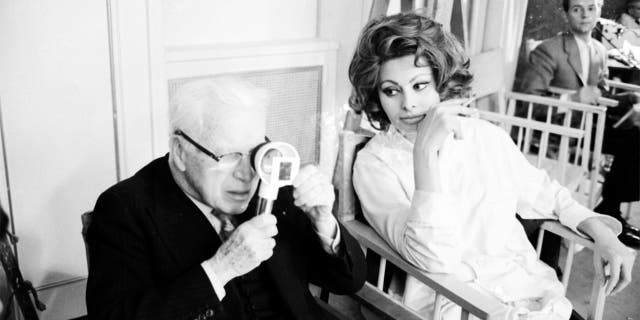 Charlie Chaplin looking a film negative through a magnifying glass while sitting close to actress Sophia Loren during filming on the set of the movie 'A Countess from Hong Kong' at the Pinewood Studios in London, 1966