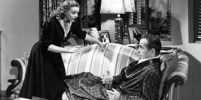 Martha Stewart talks to Humphrey Bogart who's lying on the couch in a scene from the film 'In a Lonely Place', 1950.
