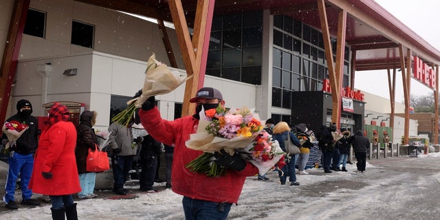 An HEB grocery store employee hands out flowers to customers waiting in line in the snow Thursday in Austin, Texas. (AP)