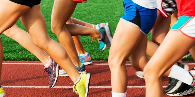 A girls cross country team running on a red track at the start of practice on a early summer evening.