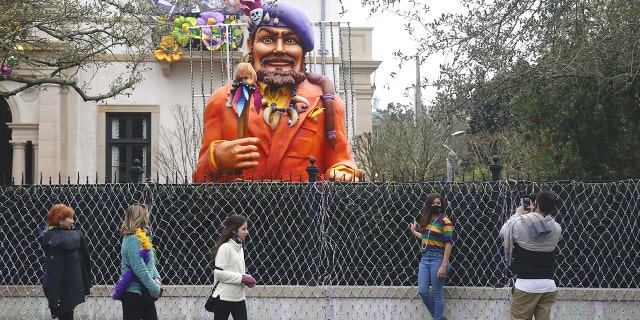 Passersby stop for photos in front of a house decorated for Mardi Gras.