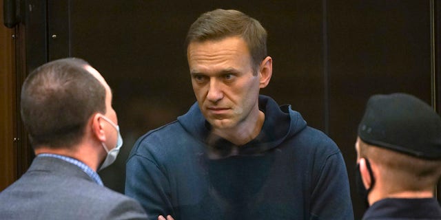 In this handout photo provided by Moscow City Court Russian opposition leader Alexei Navalny talks to one of his lawyers, left, while standing in the cage during a hearing to a motion from the Russian prison service to convert the suspended sentence of Navalny from the 2014 criminal conviction into a real prison term in the Moscow City Court in Moscow, Russia, Tuesday, Feb. 2, 2021. (Moscow City Court via AP)