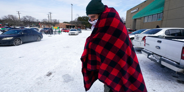 Cody Jennings uses a blanket to keep warm outside a grocery store Tuesday, Feb. 16, 2021, in Dallas.