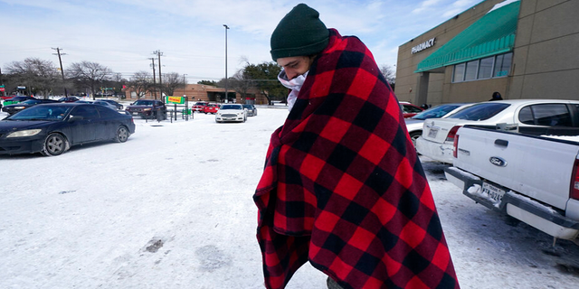 Cody Jennings uses a blanket to keep warm outside a grocery store Tuesday, Feb. 16, 2021, in Dallas.