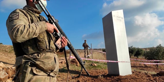 Turkish police officers guard a monolith, found on an open field near Sanliurfa, southeastern Turkey, Sunday, Feb. 7, 2021. The metal block was found by a farmer Friday in Sanliurfa province with old Turkic script that reads "Look at the sky, see the moon." The monolith, 3 meters high (about 10 feet), was discovered near UNESCO World Heritage site Gobeklitepe with its megalithic structures dating back to 10th millennium B.C. Turkish media reported Sunday that gendarmes were looking through CCTV footage and investigating vehicles that may have transported the monolith. Other mysterious monoliths have popped up and some have disappeared in numerous countries since 2020. (Bekir Seyhanli/IHA via AP)