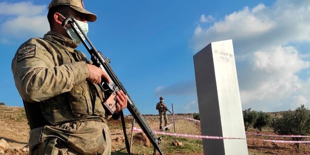 Turkish police officers guard a monolith, found on an open field near Sanliurfa, southeastern Turkey, Sunday, Feb. 7, 2021. The metal block was found by a farmer Friday in Sanliurfa province with old Turkic script that reads "Look at the sky, see the moon." The monolith, 3 meters high (about 10 feet), was discovered near UNESCO World Heritage site Gobeklitepe with its megalithic structures dating back to 10th millennium B.C. Turkish media reported Sunday that gendarmes were looking through CCTV footage and investigating vehicles that may have transported the monolith. Other mysterious monoliths have popped up and some have disappeared in numerous countries since 2020. (Bekir Seyhanli/IHA via AP)