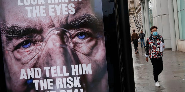 A man wearing a mask against coronavirus walks past an NHS advertisement about COVID-19 in London, Tuesday, Feb. 2, 2021.  (AP Photo/Alastair Grant)