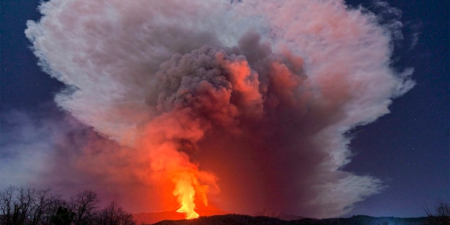 A fiery river of glowing lava flows on the north-east side of the Mt Etna volcano engulfed with ashes and smoke near Milo, Sicily, Wednesday night, Feb. 24, 2021.  (AP Photo/Salvatore Allegra)