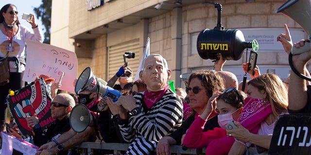 Protesters, including one wearing a mask depicting Israeli Prime Minister Benjamin Netanyahu, gather outside the District Court during a hearing in his corruption trial, in Jerusalem, Monday, Feb. 8, 2021. (AP Photo/Maya Alleruzzo)