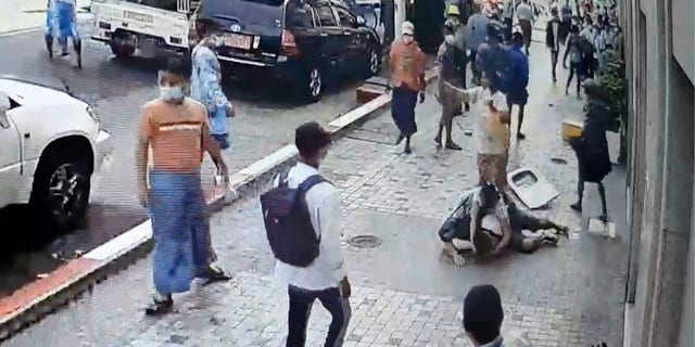 In this image taken from video obtained by Than Lwin Khet News, a woman helps an unidentified man lying on the sidewalk of Sule Pagoda Road after he was attacked by a group of men in Yangon, Burma, on Thursday. (Than Lwin Thet News via AP)