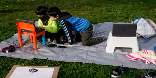 Clarendon Alternative Elementary School second graders Yaichiro Tanaka, left, and Haruki Ishiyama look at a computer screen as students and parents attend distance learning Zoom classes at Midtown Terrace Playground in San Francisco, on Thursday. (AP)