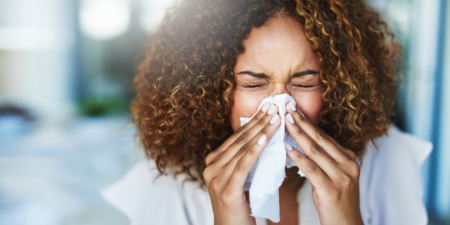 A woman sneezes into a tissue. Dr. Parikh recommended that cat owners keep their feline friends out of the bedroom.
