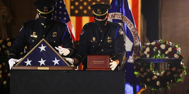 An honor guard places an urn with the cremated remains of U.S. Capitol Police officer Brian Sicknick and folded flag on a black-draped table at center of the Capitol Rotunda to lie in honor Tuesday, Feb. 2, 2021, in Washington. (Leah Millis/Pool via AP)