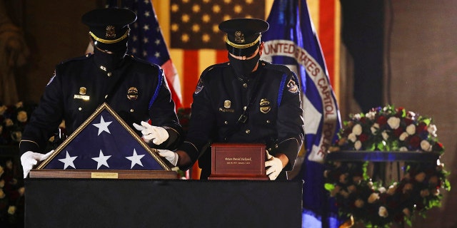 An honor guard places an urn with the cremated remains of U.S. Capitol Police officer Brian Sicknick and folded flag on a black-draped table at center of the Capitol Rotunda to lie in honor Tuesday, Feb. 2, 2021, in Washington. (Leah Millis/Pool via AP)