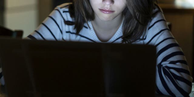 Young girl is crying lonely with tears in front of her laptop late at night (iStock)