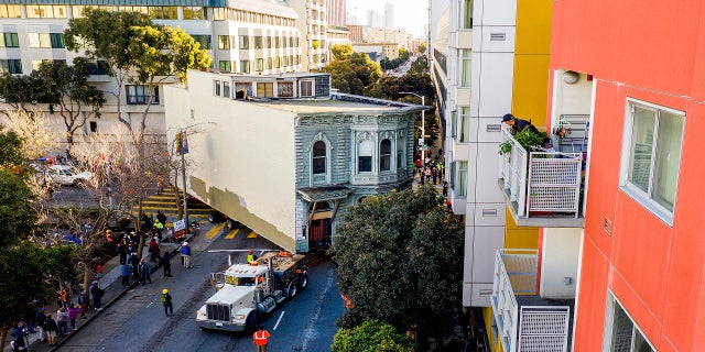A man watches from a balcony as a truck pulls a Victorian home through San Francisco on Sunday. (AP)