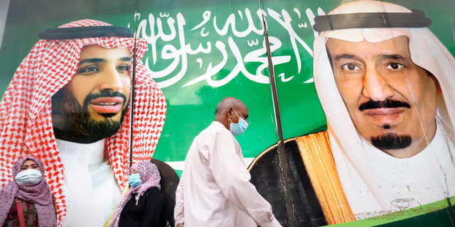 People wear face masks to protect against the spread of the coronavirus in front of a banner showing Saudi King Salman, right, and his Crown Prince Mohammed bin Salman, outside a mall in Jeddah, Saudi Arabia, on Friday, Feb. 5. (AP)