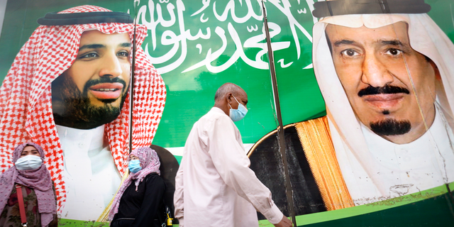 People wear face masks to protect against the spread of the coronavirus in front of a banner showing Saudi King Salman, right, and his Crown Prince Mohammed bin Salman, outside a mall in Jeddah, Saudi Arabia, on Friday, Feb. 5. (AP)