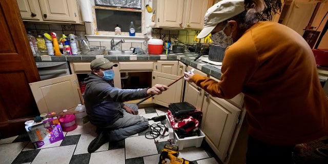Handyman Roberto Valerio, left, hands homeowner Nora Espinoza a broken pipe after removing it from beneath her kitchen sink on Saturday in Dallas. The pipe broke during freezing temperatures brought by last week's winter weather. (AP)