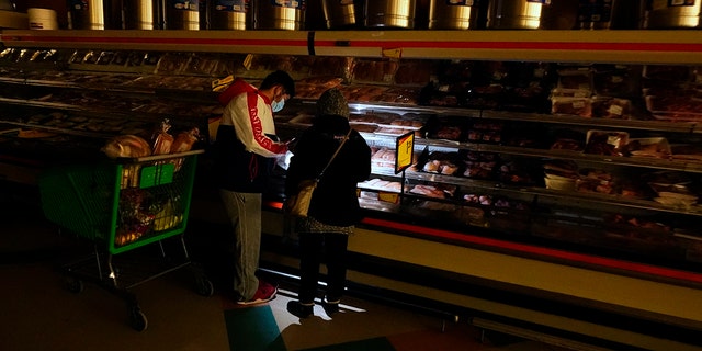 Customers use a cell phone light to look in the meat section of a grocery store on Tuesday, February 16, 2021 in Dallas.  Even though the store lost power, it was open for cash sales only.