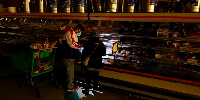 Customers use the light from a cell phone to look in the meat section of a grocery store Tuesday, Feb. 16, 2021, in Dallas. Even though the store lost power, it was open for cash only sales.