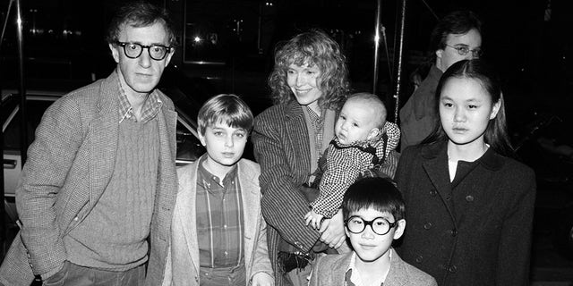 American comedian, actor and film director Woody Allen (left) and his partner, actress Mia Farrow, pose under a canopy with their children, from left Misha, Dylan (in Farrow's arms), Fletcher and Soon Yi, New York, New York, 1986. Soon-Yi later married Allen.  The man in the background has not been identified. 