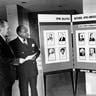 A full-length portrait of Alan K. Campbell, director, left, and Dr. J Rupert Picott, executive director of the US Office of Personnel Management Headquarters, standing next to a Black History Month exhibit and holding a copy of President Carter's statement, Washington, D.C., 1976.