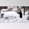 A man brushes snow off a car, Tuesday, Feb. 2, 2021, in Lawrence, Mass. A sprawling, lumbering winter storm has walloped the Eastern U.S., shutting down coronavirus vaccination sites, closing schools and halting transit.