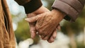 Close up of elderly couple holding hands and walking outdoors. Rear view of man and woman holding hands of each other while walking outdoors.