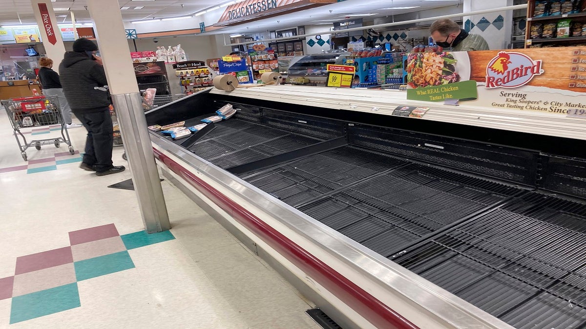 The refrigerated case for packages of chicken is almost empty as a shopper passes by late Thursday in a grocery store in south Denver. Grocers have been overrun by shoppers as they prepare to possibly be homebound for several days as a major storm targets the intermountain West. (AP)