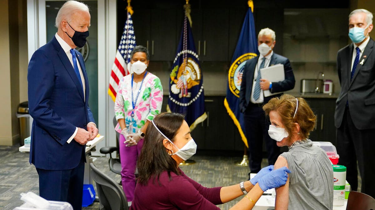 President Joe Biden, standing left, visits a COVID-19 vaccination site and watches as Dr. Navjit Goraya gives a vaccine to Air Force Col.