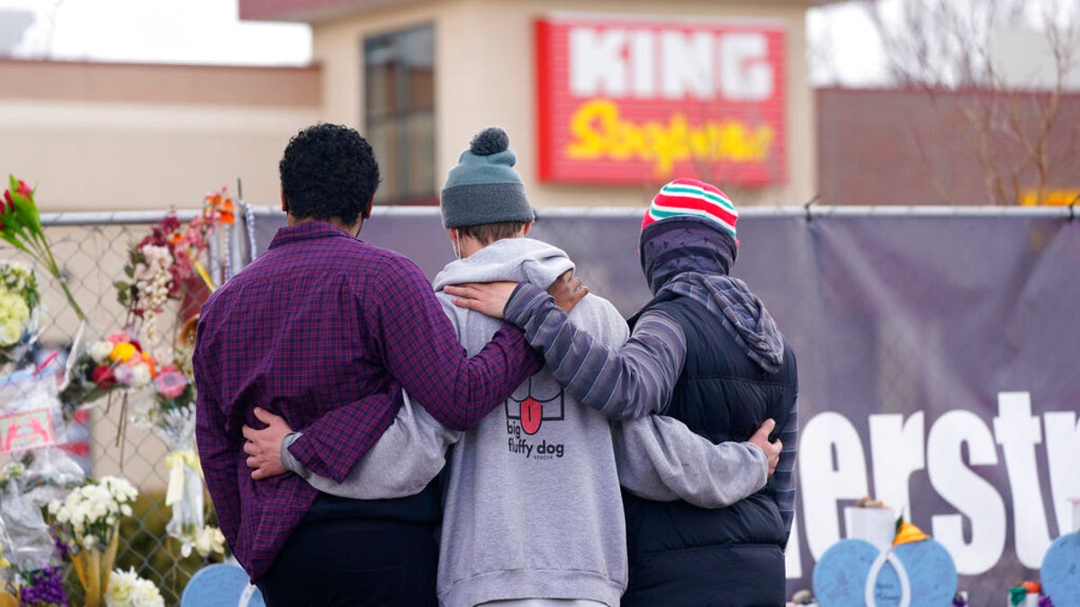 Mourners console each other along the temporary fence line outside the parking lot of a King Soopers grocery store, the site of a mass shooting in which 10 people died, Friday, March 26, 2021, in Boulder, Colo.