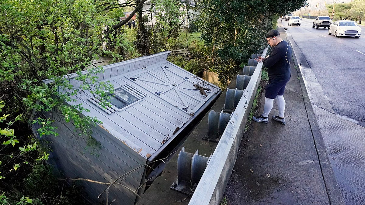 Adam Wirdzek stops to look at a utility building that was carried down a flooded creek Sunday, March 28, 2021, in Nashville, Tenn. Heavy rain across Tennessee flooded homes and roads as a line of severe storms crossed the state. (AP Photo/Mark Humphrey)