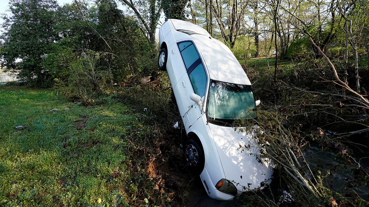 A car that was carried by floodwaters leans against a tree in a creek Sunday, March 28, 2021, in Nashville, Tenn. Heavy rain across Tennessee flooded homes and roads as a line of severe storms crossed the state. (AP Photo/Mark Humphrey)
