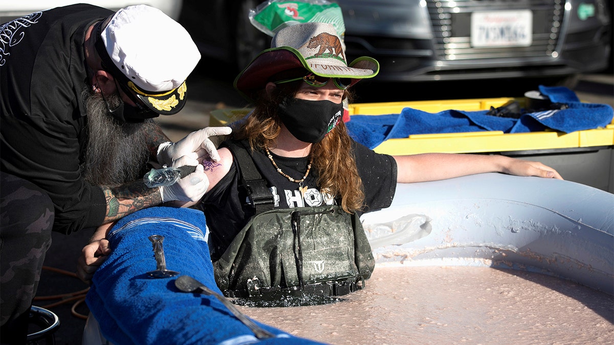 Stuntman Hunter Ray Barker gets a logo of Lor Toros restaurant tattooed on his arm as he sits partially submerged in a bean dip tub in Chatsworth, California.