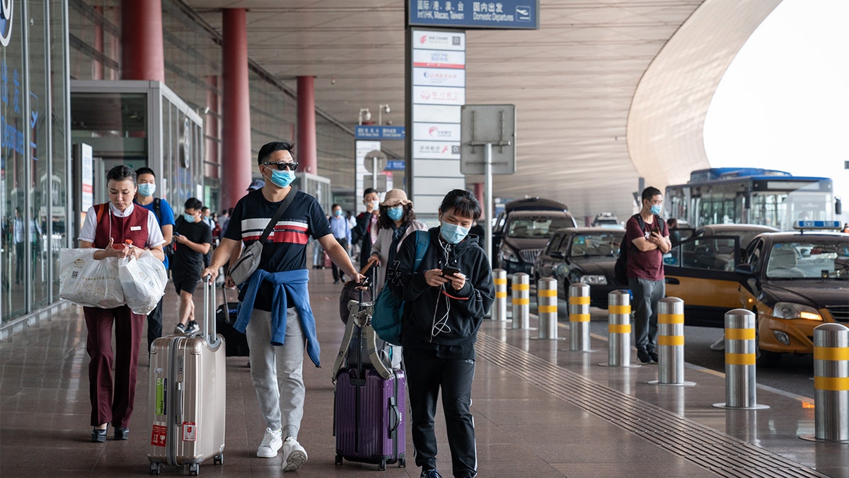 Travelers wearing protective masks push their luggage outside Beijing Capital International Airport in Beijing, China, on Wednesday, Sept. 30, 2020. (Yan Cong/Bloomberg via Getty Images)