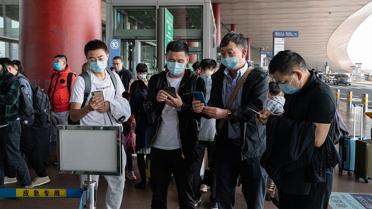 Travelers wearing protective masks use their smartphones to scan a QR code before entering Beijing Capital International Airport in Beijing, China, on Wednesday, Sept. 30, 2020. (Yan Cong/Bloomberg via Getty Images)