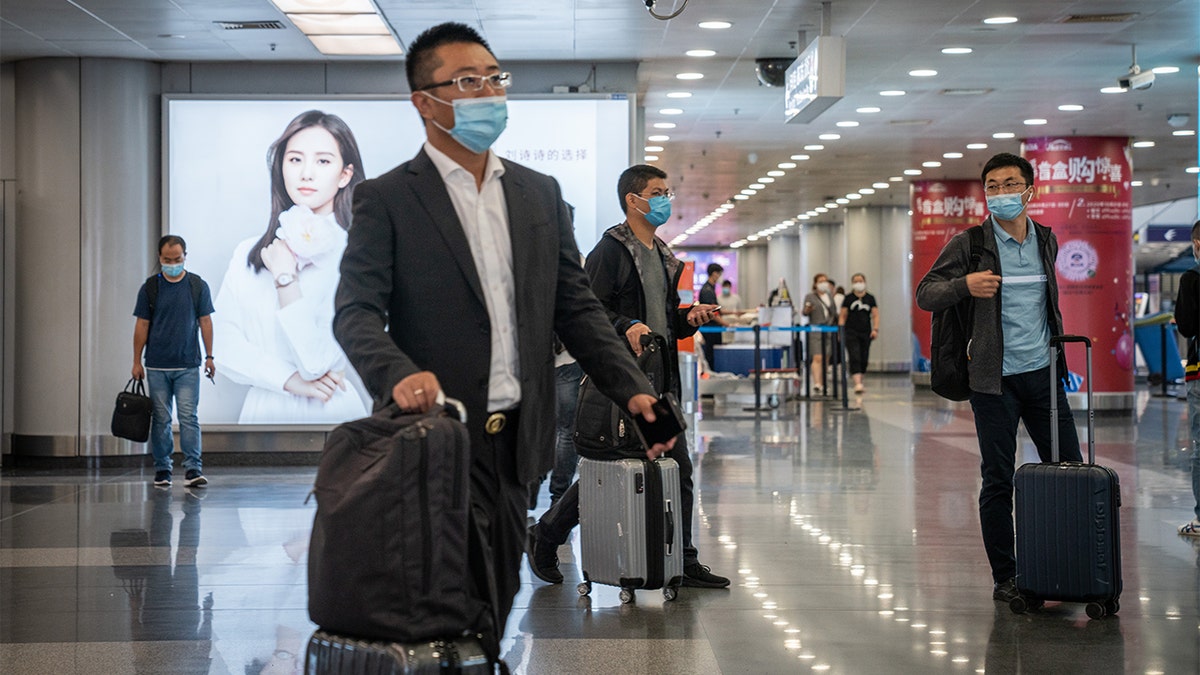 Travelers wearing protective masks push their luggage through Beijing Capital International Airport in Beijing, China, on Wednesday, Sept. 30, 2020. (Yan Cong/Bloomberg via Getty Images)