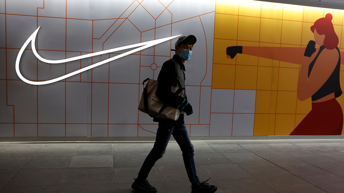 A visitor to a mall wearing a mask past by a Nike store in Beijing on Monday, March 29, 2021. China stepped up pressure Monday on foreign shoe and clothing brands to reject reports of abuses in Xinjiang, telling companies that are targeted by Beijing for boycotts to look more closely and pointing to a statement by one that it found no forced labor. (AP Photo/Ng Han Guan)