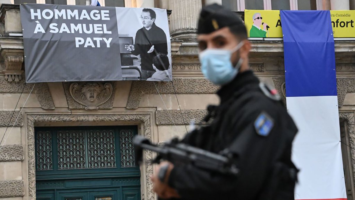 A French police officer stands next to a portrait of French teacher Samuel Paty on display on the facade of the Opera Comedie in Montpellier on October 21, 2020, during a national homage to the teacher who was beheaded for showing cartoons of the Prophet Mohamed in his civics class. - France pays tribute on October 21 to a history teacher beheaded for showing cartoons of the Prophet Mohamed in a lesson on free speech, an attack that has shocked the country and prompted a government crackdown on radical Islam. Seven people, including two schoolchildren, will appear before an anti-terror judge for a decision on criminal charges over the killing of 47-year-old history teacher Samuel Paty. (Photo by Pascal GUYOT / AFP) (Photo by PASCAL GUYOT/AFP via Getty Images)