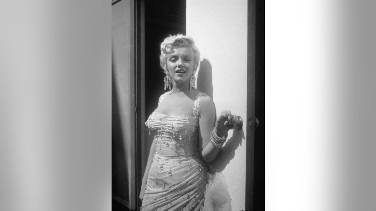 Portrait of Marilyn Monroe in a light-colored, beaded gown, as she leans against an open trailer door on the 20th Century Fox studios set during the filming of director Walter Lang's film, 'There's No Business Like Show Business,' 1954.