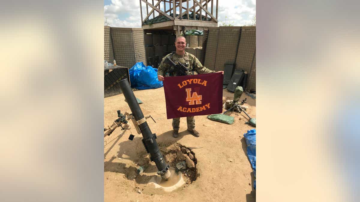 SPC George Kemper holds a Loyola Academy flag while serving in the U.S. Army.