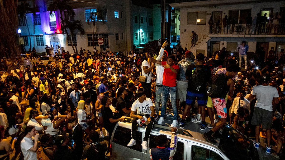 Crowds defiantly gather in the street while a speaker blasts music an hour past curfew in Miami Beach, Fla., on Sunday, March 21, 2021. An 8 p.m. curfew was extended in Miami Beach after law enforcement worked to contain unruly crowds of spring break tourists.