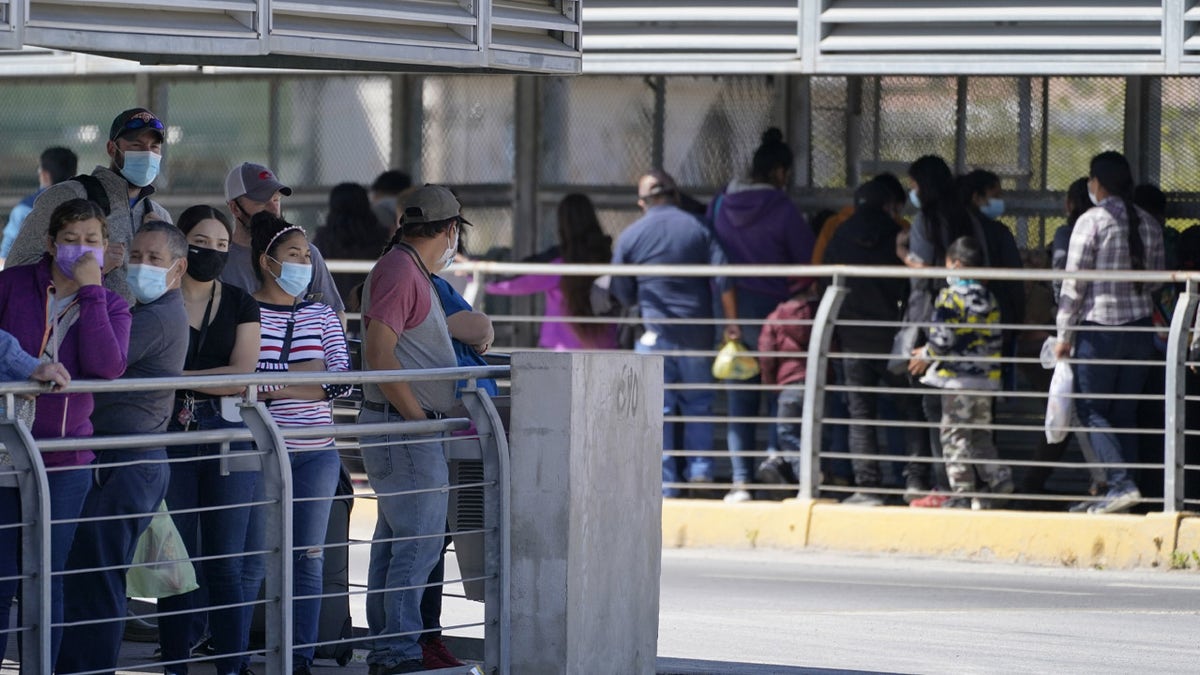 Travelers, left, waiting in line to cross a customs area into the United States at the McAllen-Hidalgo International Bridge look on as a group of migrants, right, are deported to Reynosa, Mexico. (AP Photo/Julio Cortez)