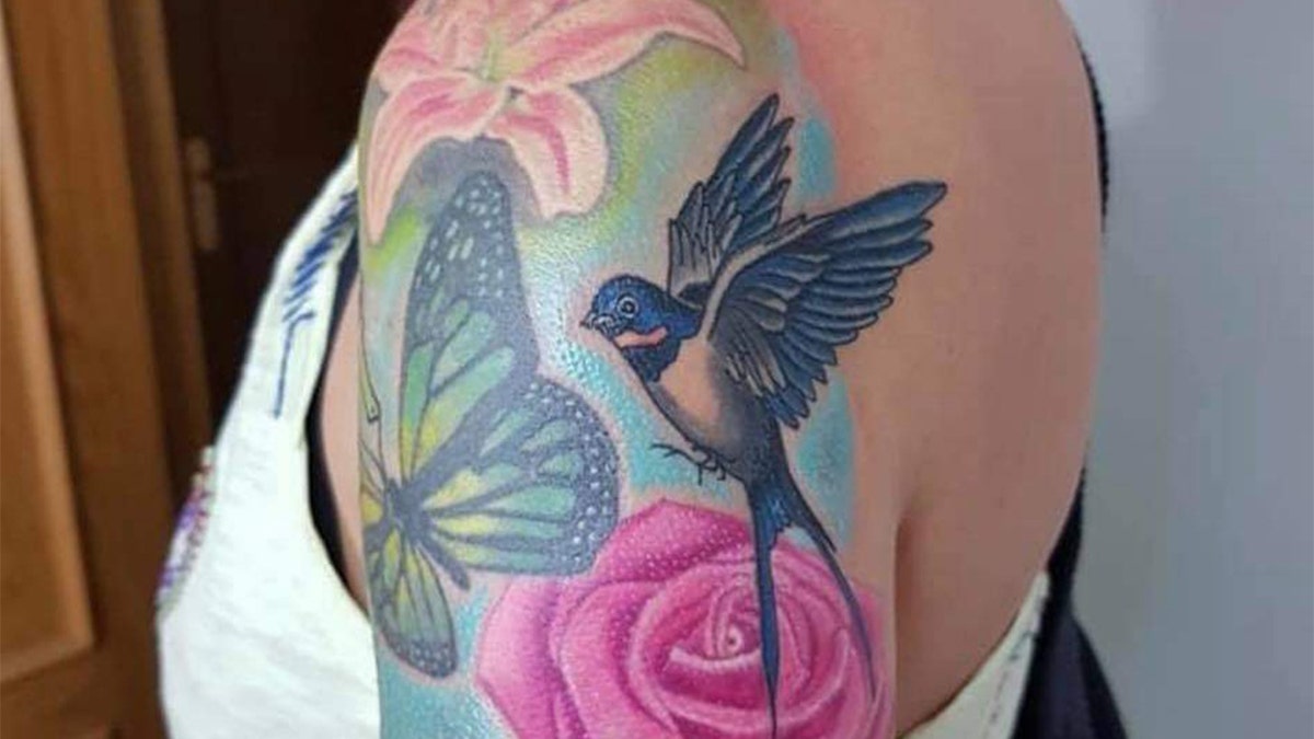 Pink flower with bird and butterfly tattoo on a woman's shoulder