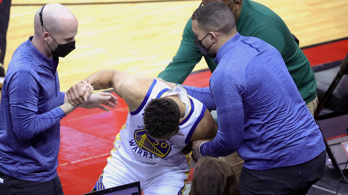 Golden State Warriors' Stephen Curry is helped by staff after falling into the Houston Rockets bench during the third quarter of an NBA basketball game Wednesday, March 17, 2021, in Houston. 